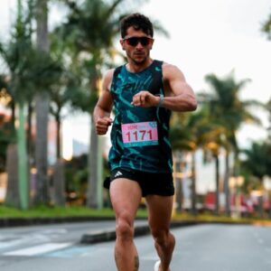Adult male athlete running in a marathon on a sunny day with palm trees in the background.
